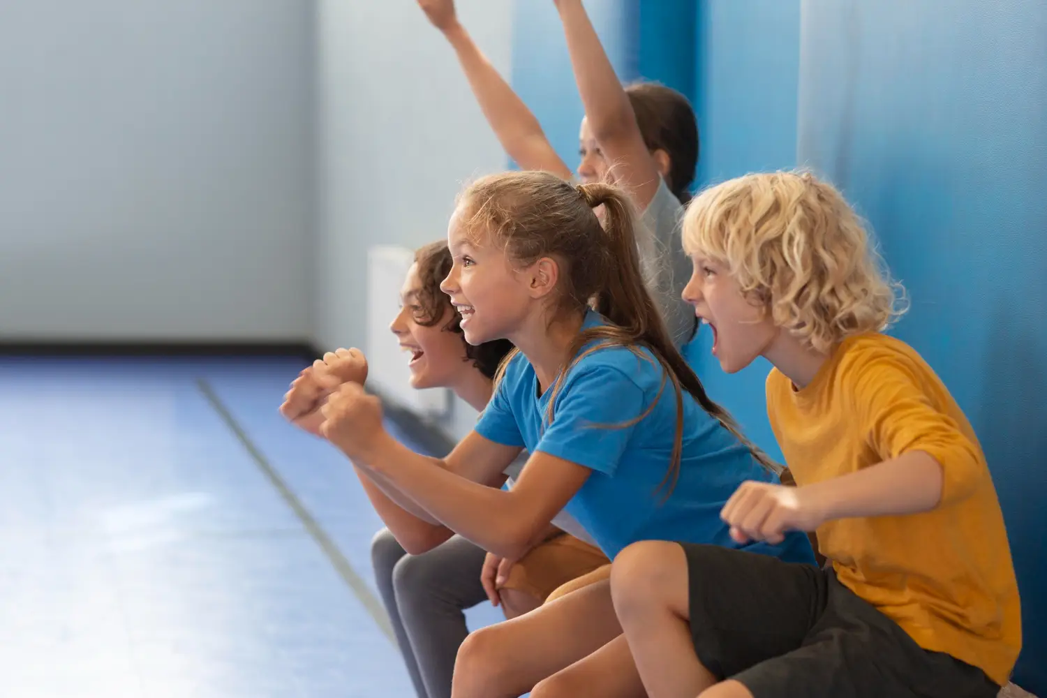 Groupe d’enfants assis dans une salle de sport, encourageant et applaudissant avec enthousiasme