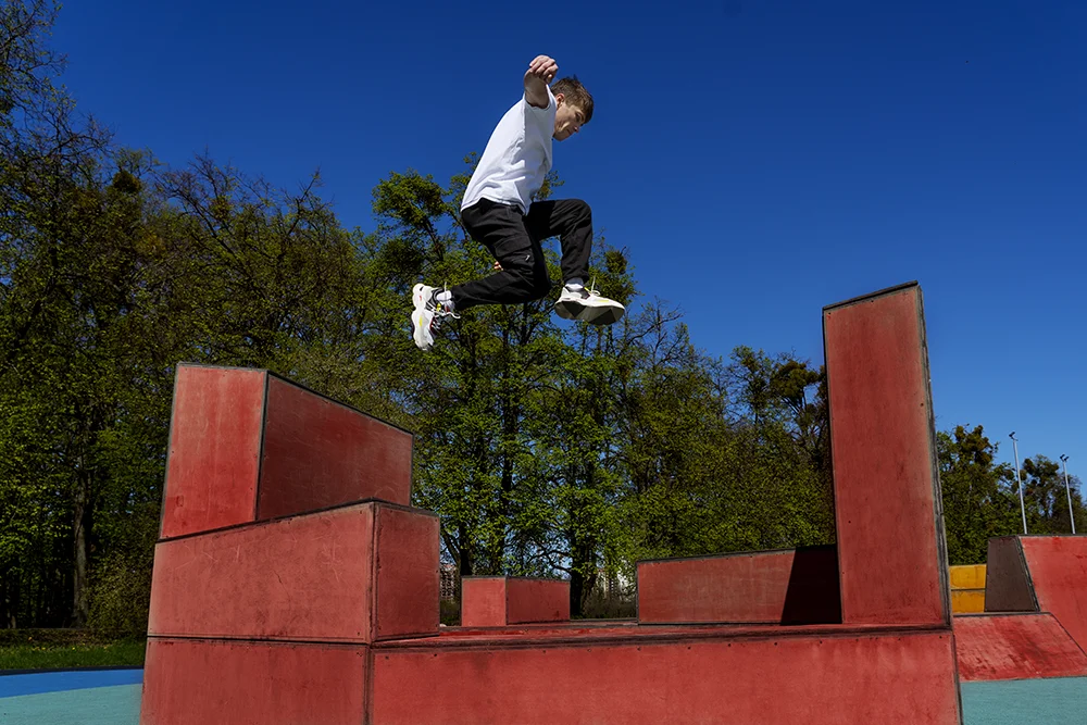 Jeune athlète effectuant un saut de parkour entre deux modules extérieurs, démontrant agilité et puissance.